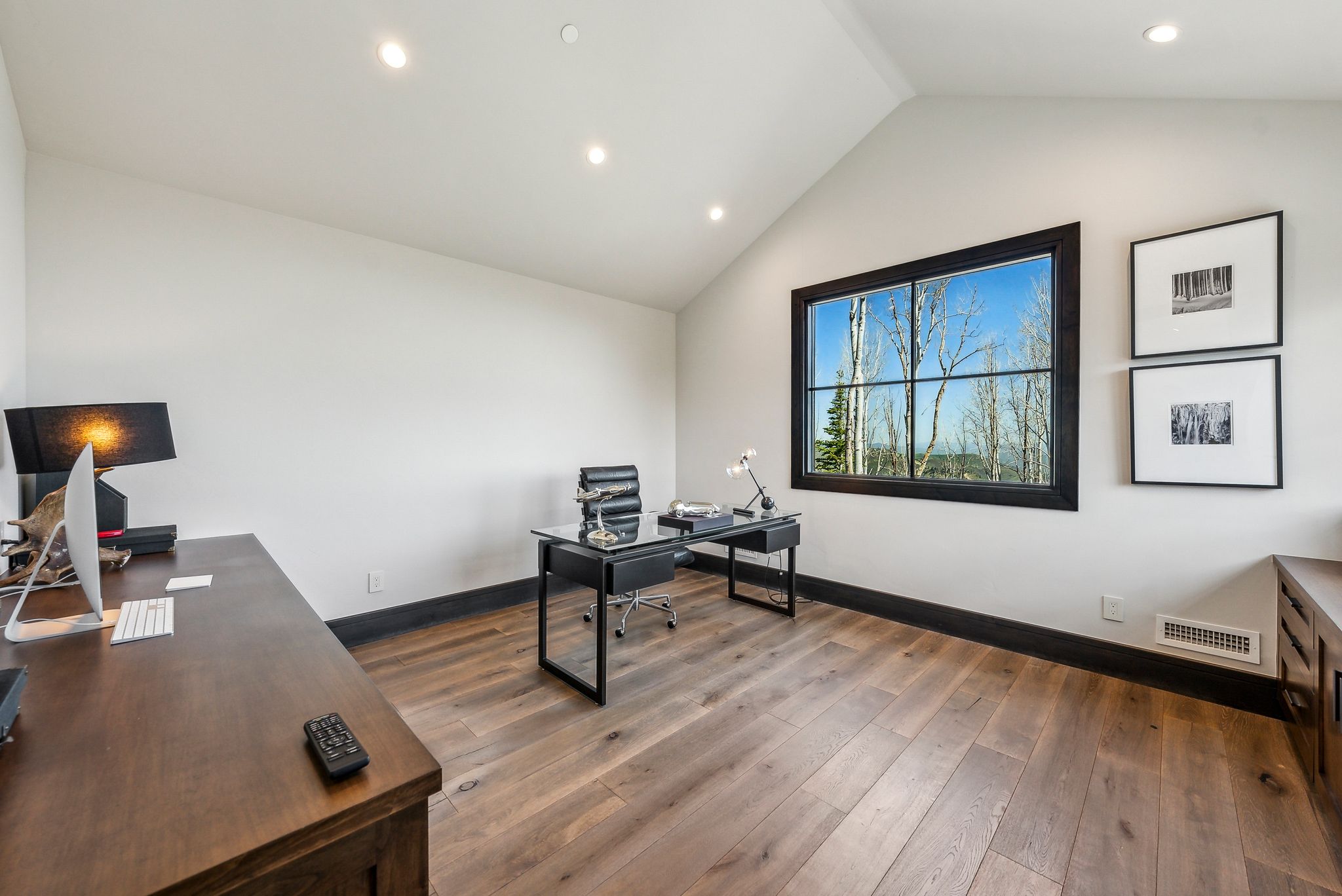 Bright interior space featuring a large window with black framing, wood-finish flooring, a vaulted ceiling, recessed lighting, and dark baseboards