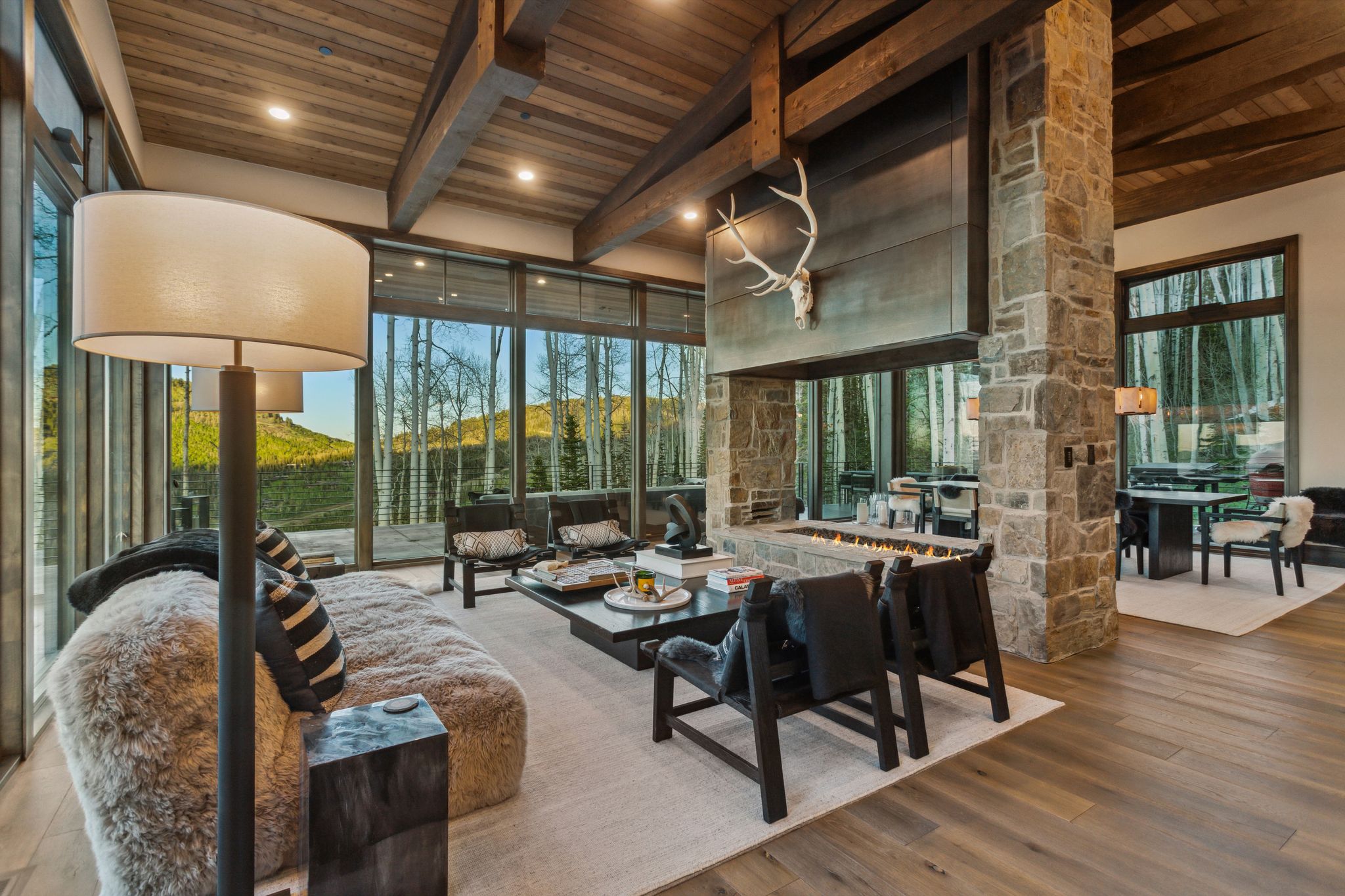 Expansive living area featuring a stone fireplace with a linear firebox, exposed wood beam ceilings, and large format windows
