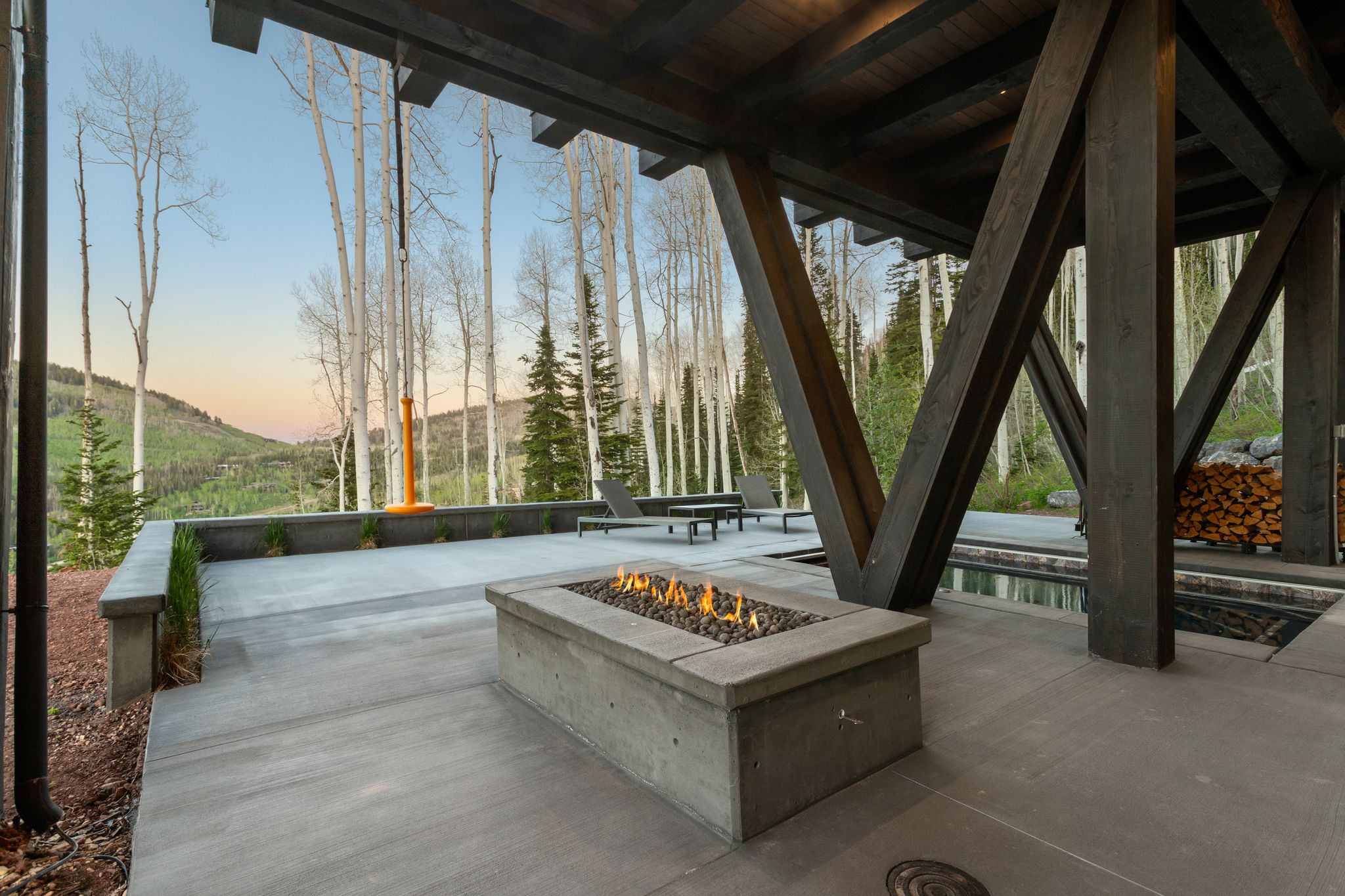Expansive concrete patio featuring a built-in fire pit, surrounded by mature aspen trees and evergreen foliage