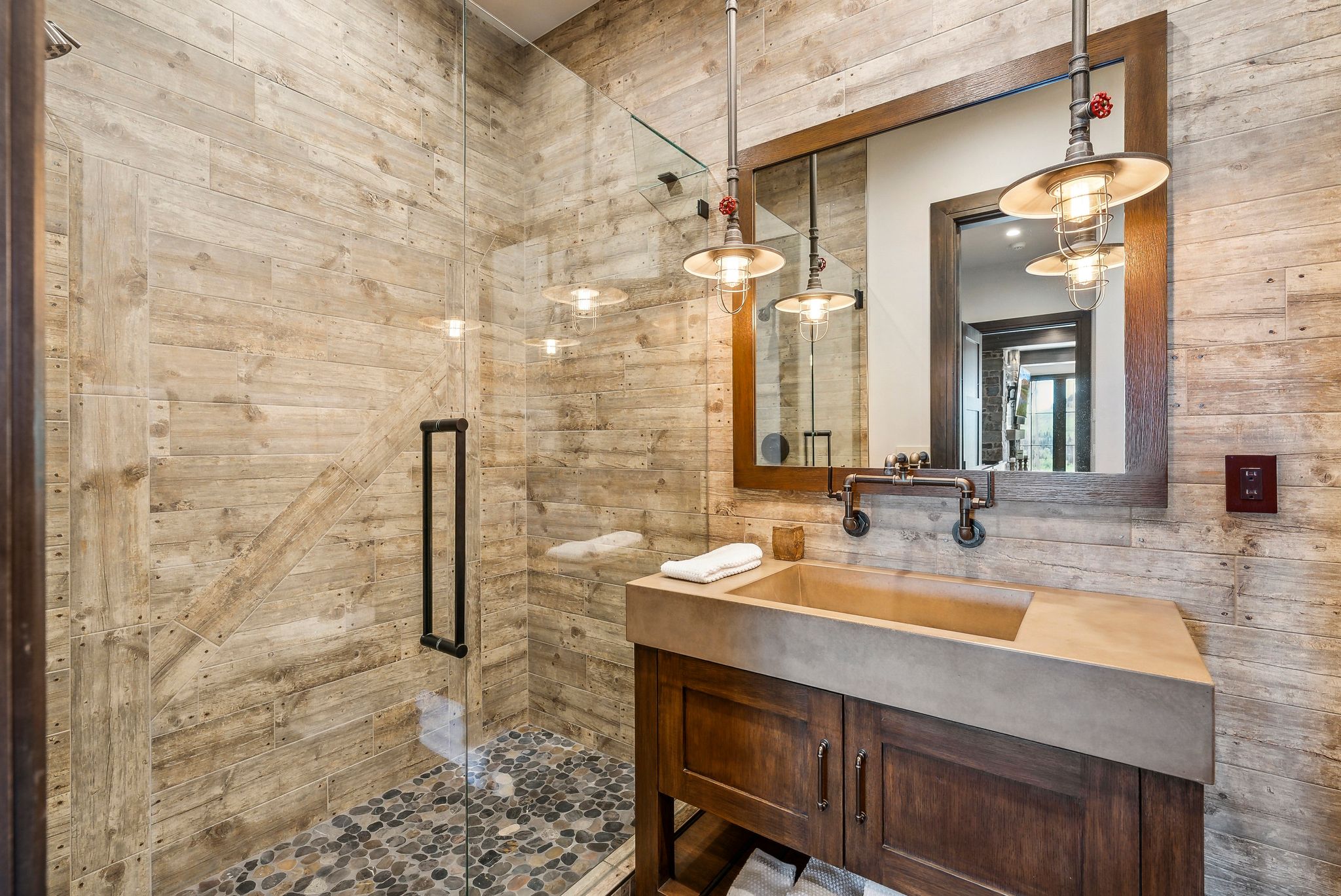 Bathroom featuring a glass-enclosed shower with pebble flooring and wood-finish tile walls