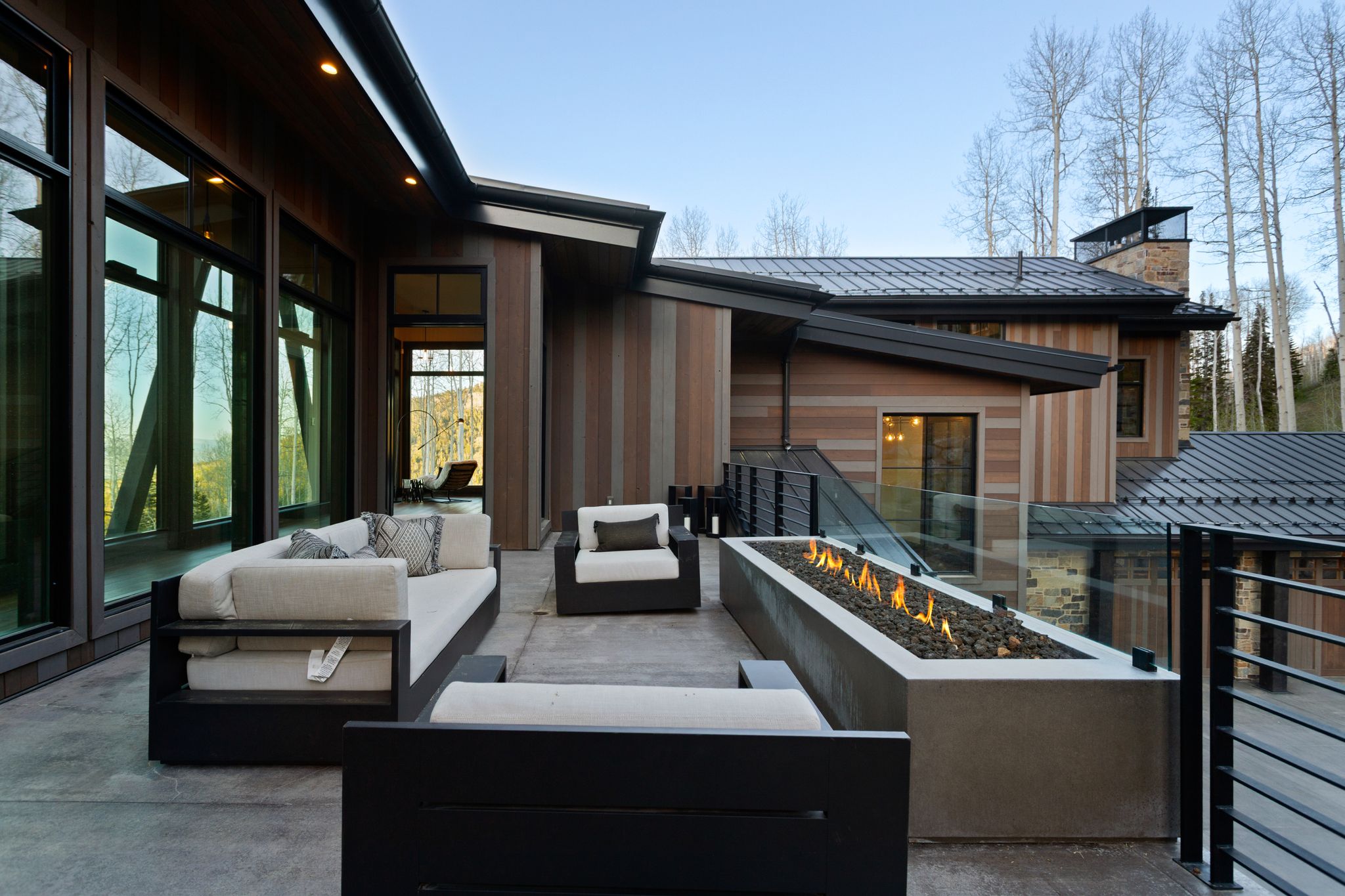 Spacious outdoor patio featuring a linear fire pit with glass enclosure, contemporary metal railings, and a wood-paneled exterior