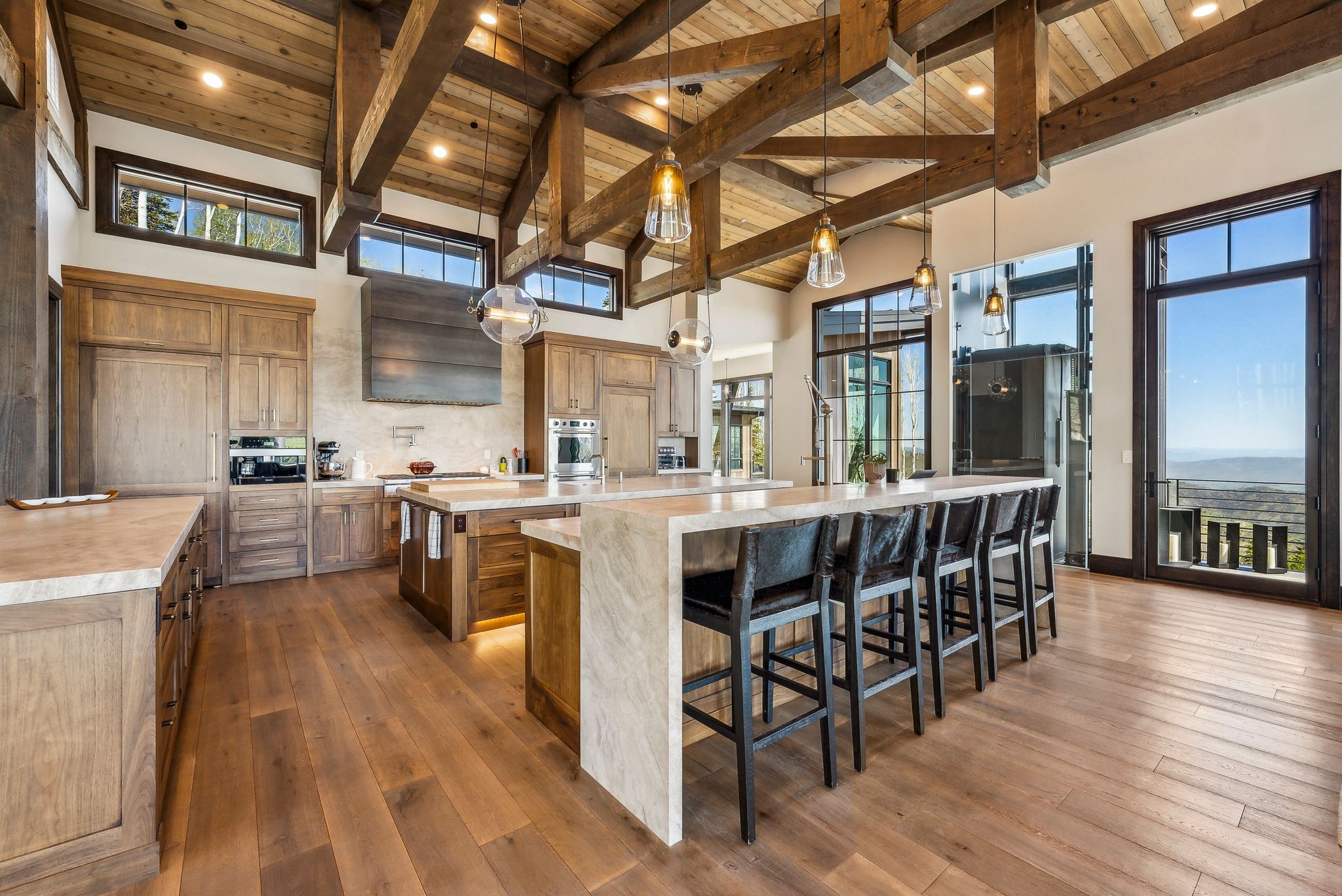 Gourmet kitchen featuring a large central island, perimeter stone countertops, integrated appliances, natural wood-finish flooring, and a vaulted ceiling with exposed beams