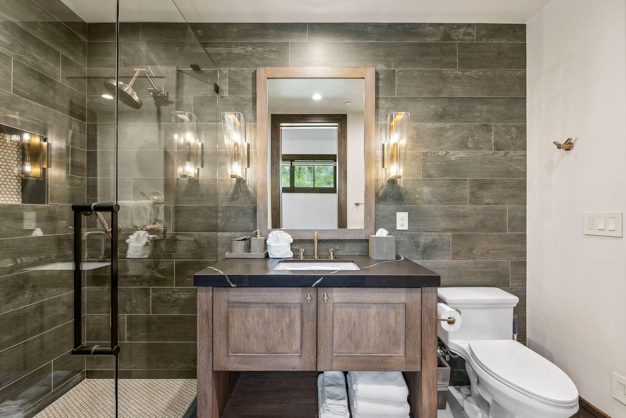 Bathroom featuring a glass-enclosed shower, wood-finish vanity with a dark countertop, rectangular undermount sink, and wall-mounted sconces