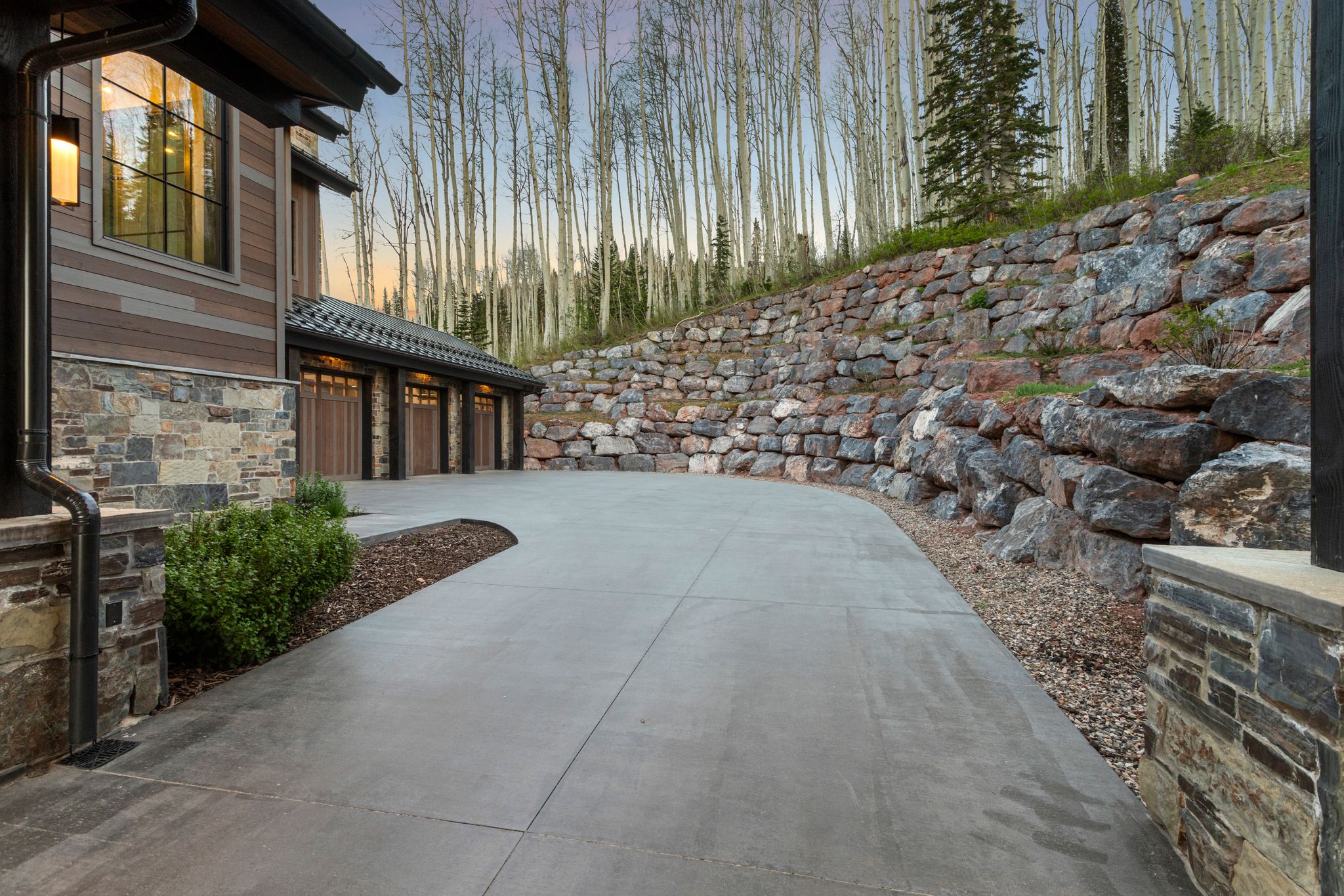 Multi-car garage featuring wood-paneled doors, stone accents, and exterior lighting