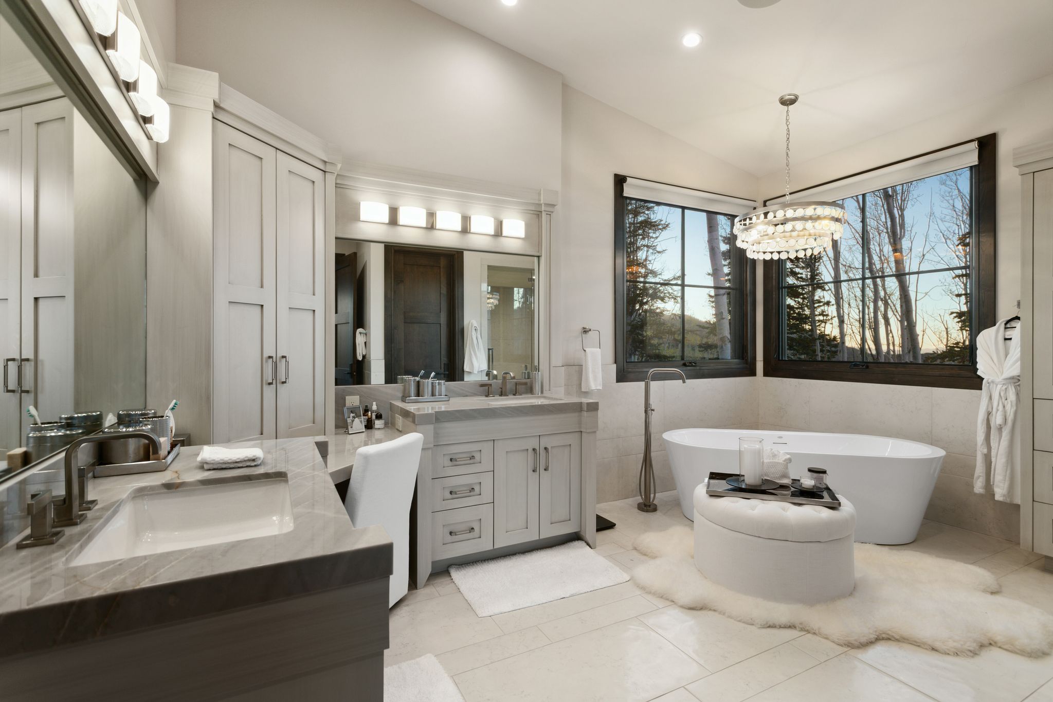 Spacious bathroom featuring a freestanding tub, dual vanities with integrated sinks, ample cabinetry, and large windows with natural scenery