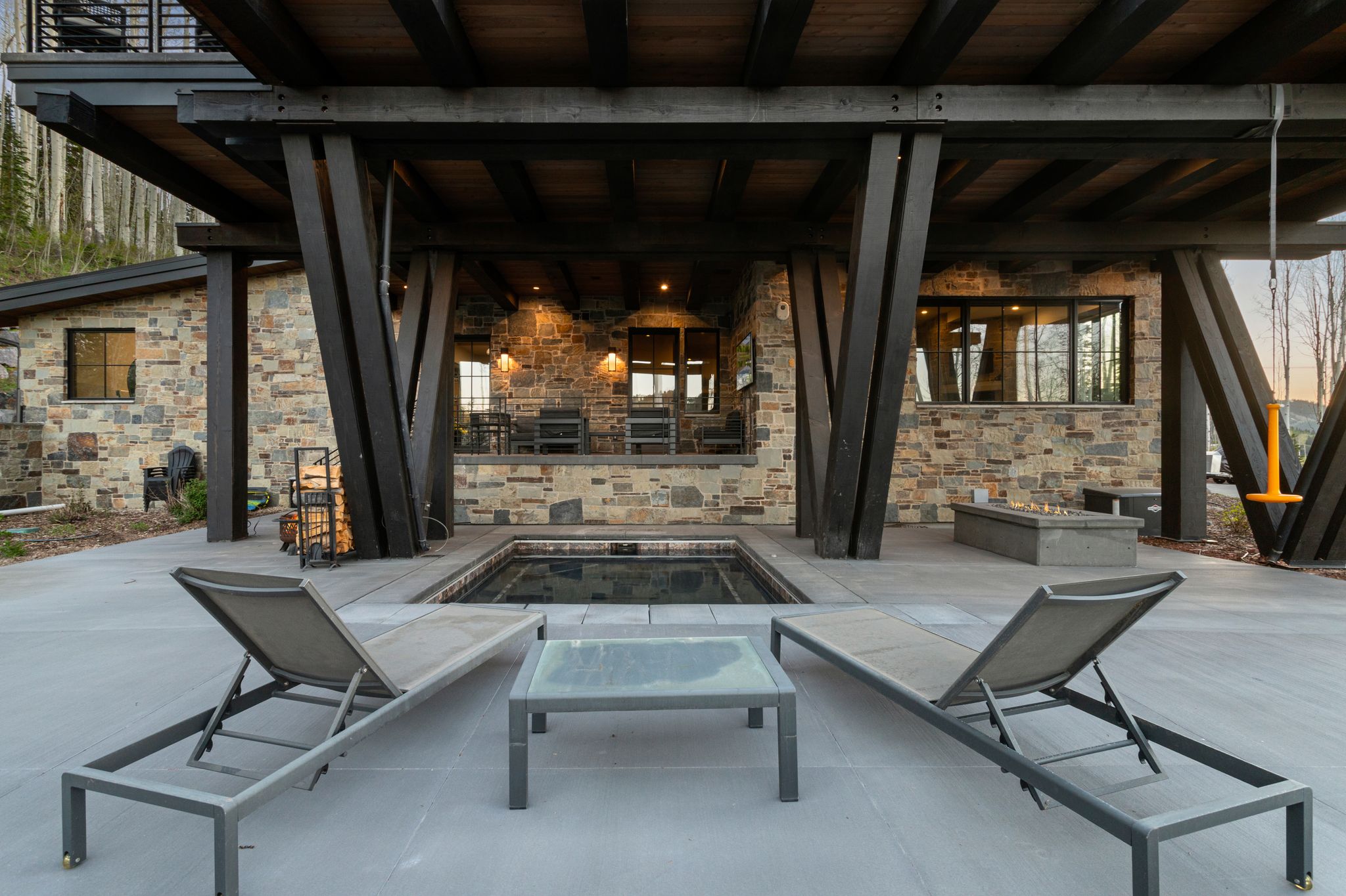 Outdoor patio featuring a built-in hot tub, concrete fire pit, and stone-clad exterior