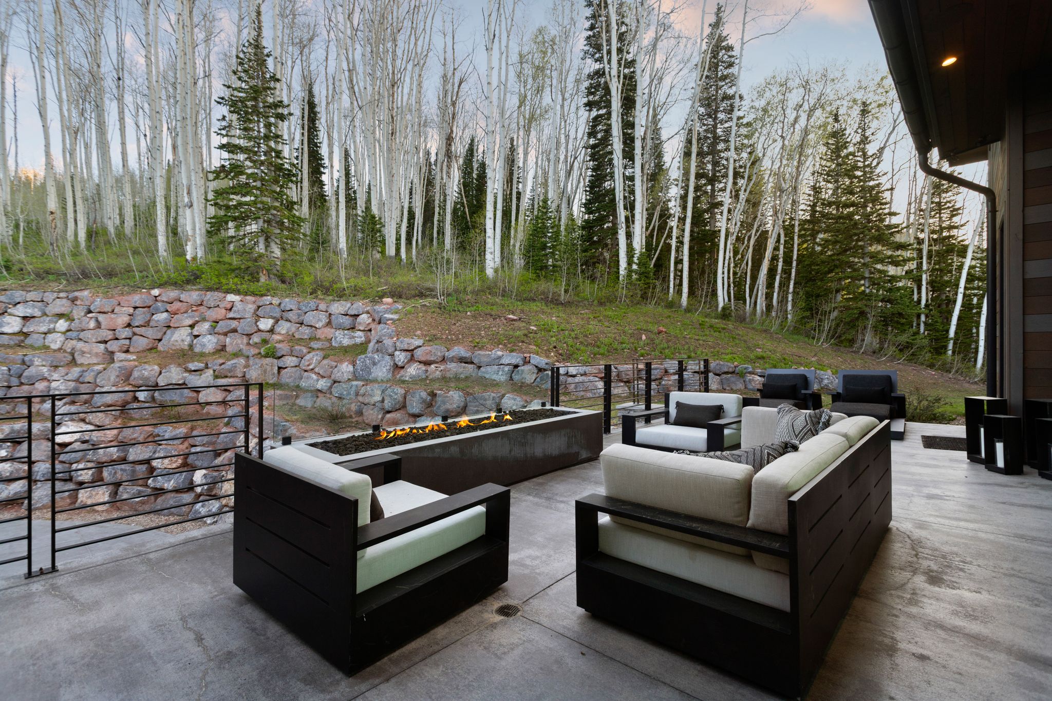 Expansive concrete patio featuring a built-in fire pit, stone retaining wall, and black metal railings