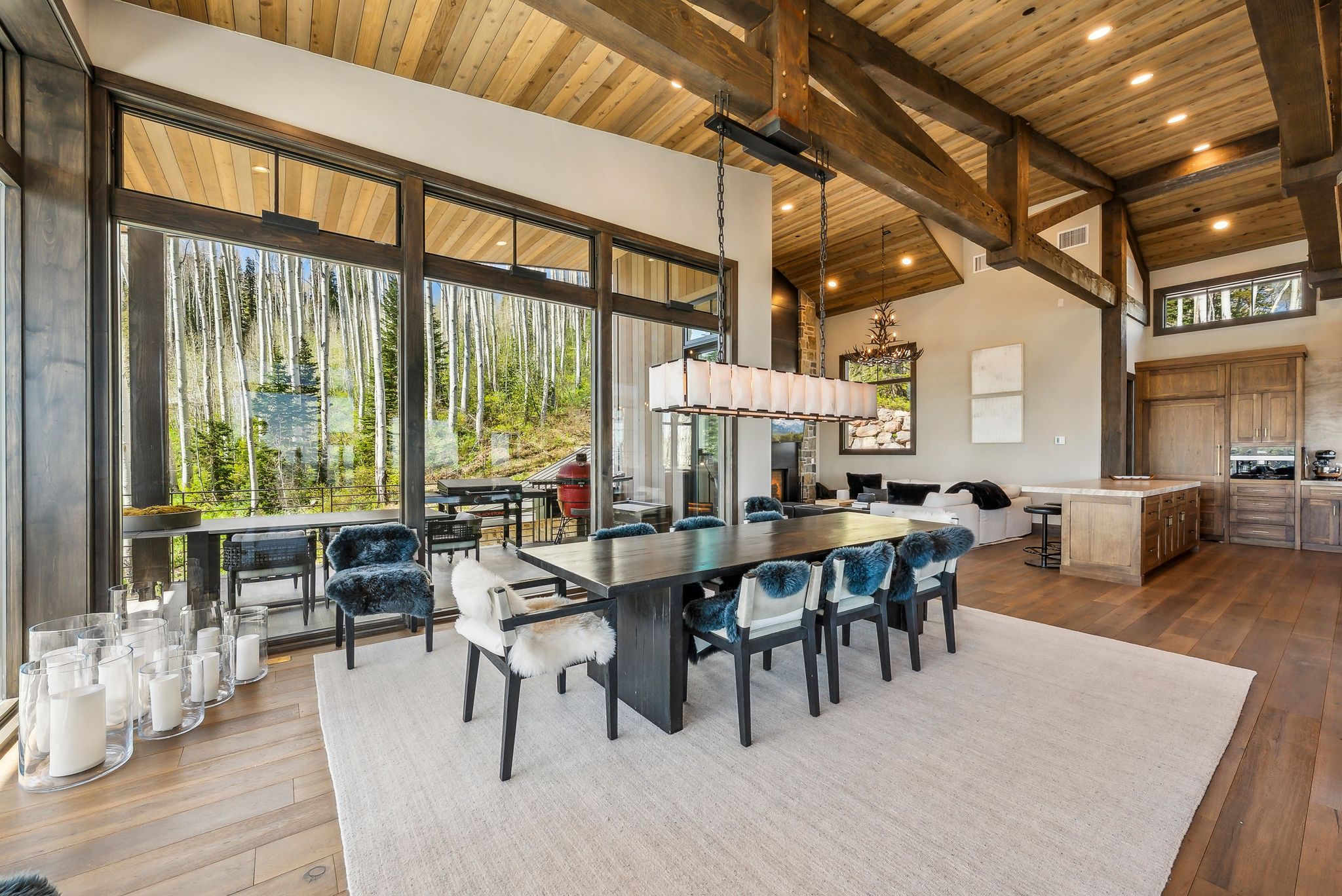 Expansive great room featuring a wood-finish vaulted ceiling with exposed beams, large format windows, wood-finish flooring, and a built-in kitchen island with stone countertop