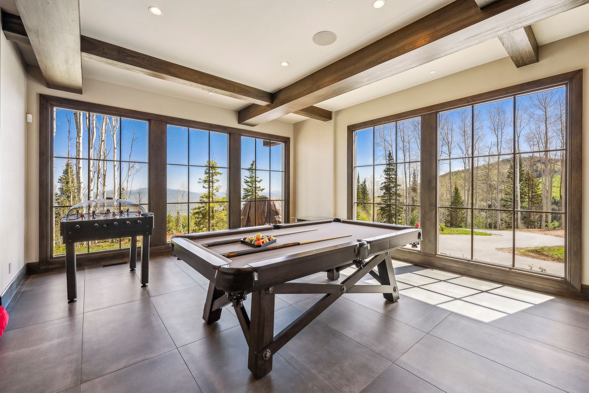 Spacious room featuring multiple large picture windows with dark trim, recessed lighting, exposed ceiling beams, and dark tile flooring