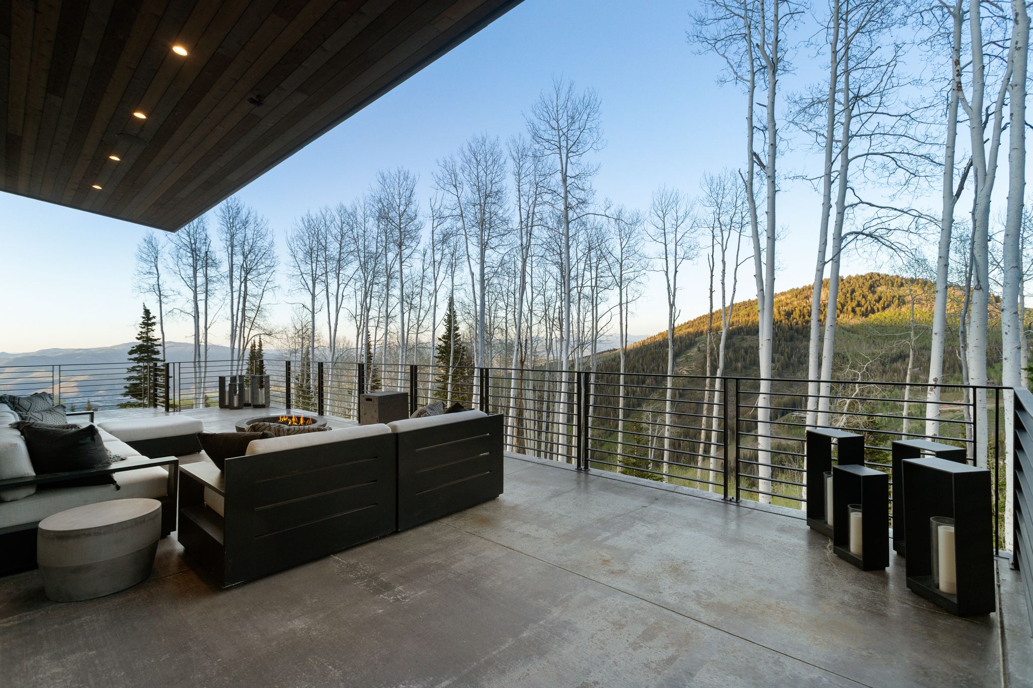 Expansive outdoor deck with concrete flooring, a linear metal railing, and a built-in fire pit