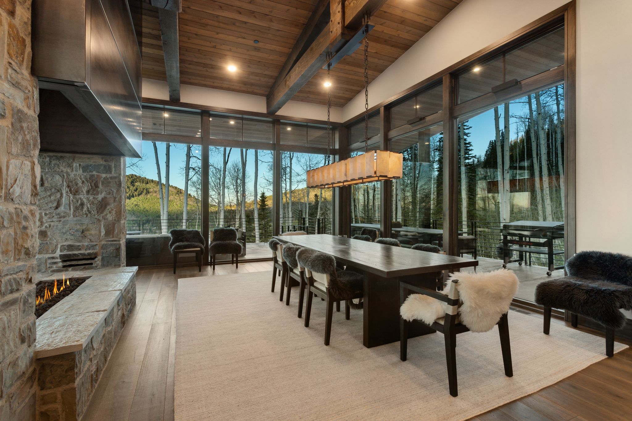 Expansive dining area featuring a full-height stone fireplace, wood-finish flooring, and a vaulted ceiling with exposed beams