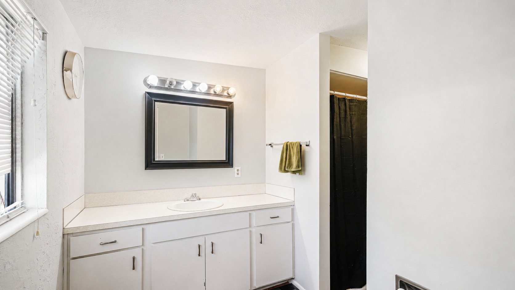 Bathroom featuring a white vanity with an integrated sink, a rectangular mirror with a black frame, and a five-bulb vanity light fixture