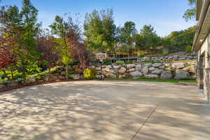 Expansive concrete driveway bordered by mature trees and a tiered rock retaining wall