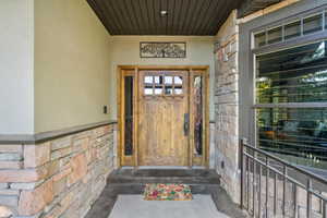 Stucco and stacked stone exterior featuring a solid wood entry door with sidelights, transom window, and dark wood soffit