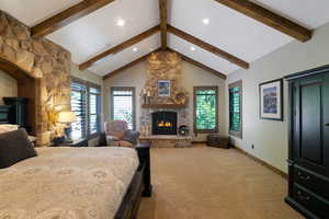 Spacious room featuring vaulted ceilings with exposed wood beams, a stone fireplace, and multiple windows with plantation shutters