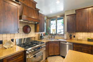 Kitchen featuring rich wood cabinetry, stone countertops, a stainless steel gas range, a dual basin sink, and a tile backsplash