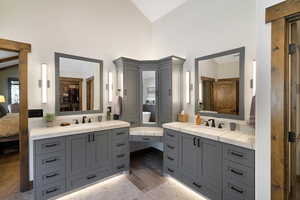Beautiful bathroom featuring gray cabinetry with matte black hardware, stone countertops, and under-cabinet lighting