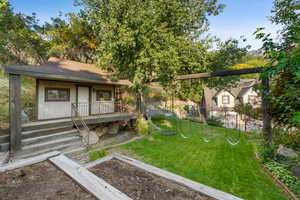 Sloped backyard featuring a green lawn, built-in swing set, and a detached structure with a front porch
