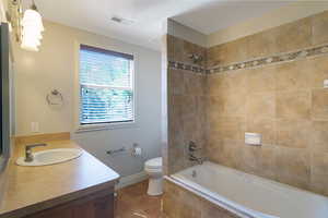 Bathroom featuring a neutral-toned vanity with an integrated sink, a window with blinds, and a tiled shower/tub combination