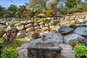 Stone patio featuring a built-in fire pit with a stone and tile surround, expansive rock retaining walls, and mature landscaping