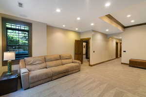 Carpeted recreation area featuring recessed lighting, a decorative wood-trimmed ceiling element, and a window with exterior tree views