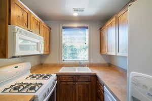 U-shaped kitchen featuring wood cabinetry, laminate countertops, a double basin sink with window, a gas range with an over-the-range microwave, and a built-in dishwasher