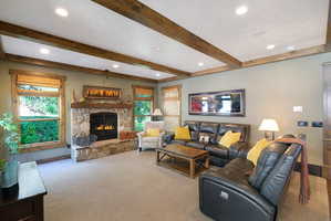 Living room featuring a stone-clad fireplace with a wood mantle, wood-beam ceiling accents, recessed lighting, and carpet flooring