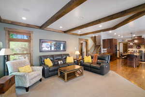 Living area featuring exposed wood beams, recessed lighting, carpet flooring, and wood-finish window trim