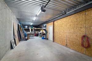 Spacious utility area featuring a concrete floor, exposed corrugated metal ceiling, and fluorescent lighting