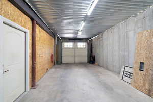 Concrete flooring and walls featuring a corrugated metal ceiling with fluorescent lighting