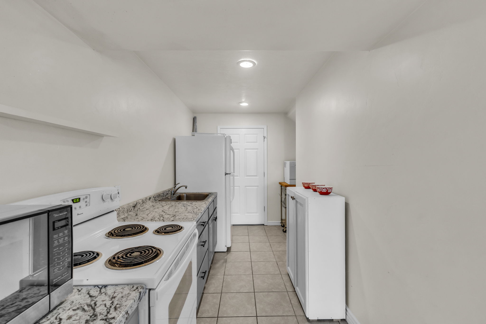 Galley-style kitchen featuring tile flooring, stone-finish countertops, built-in cabinetry, an electric range, and a full-size refrigerator