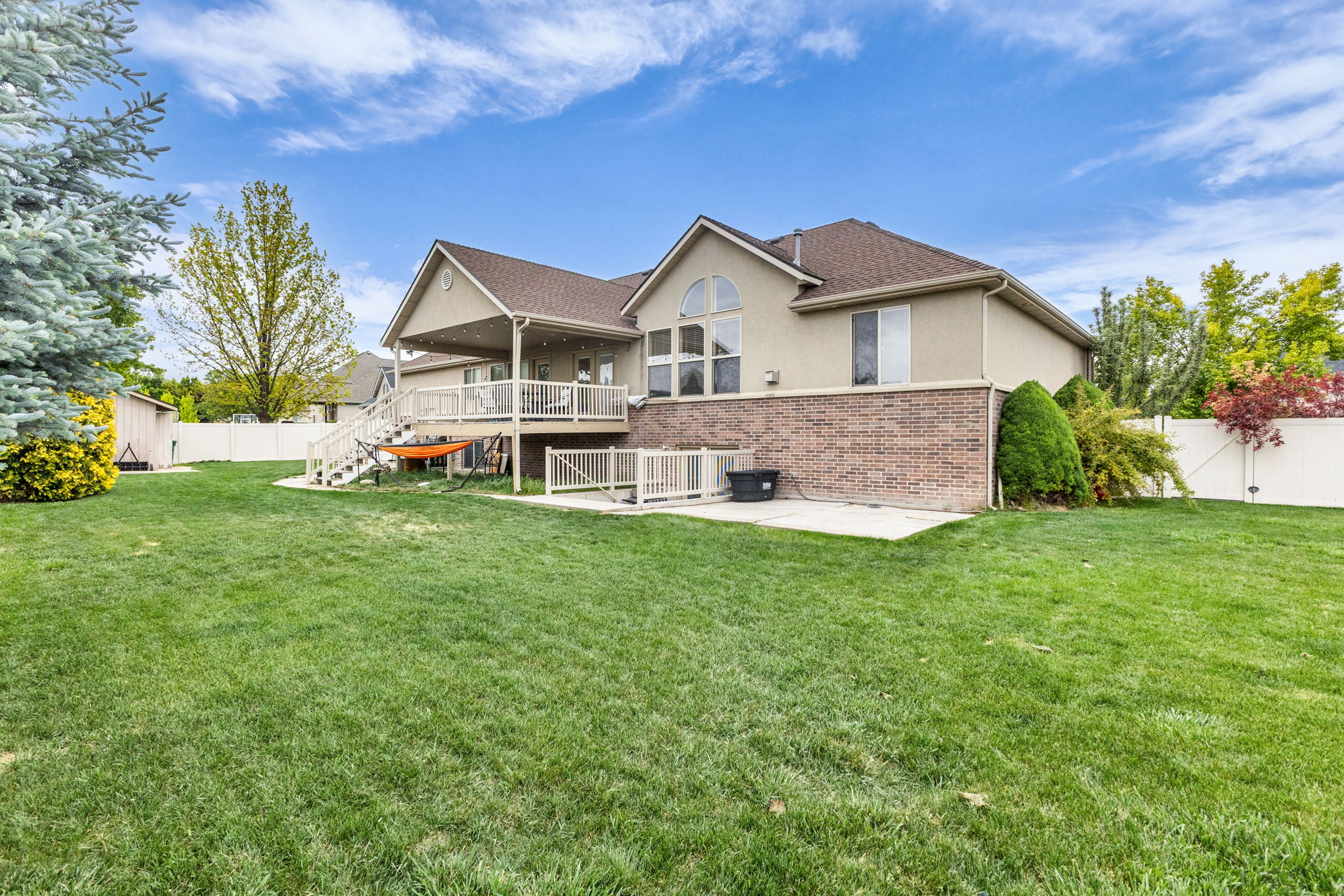 Spacious backyard featuring a manicured lawn, an elevated covered deck with white railings, and a lower patio area