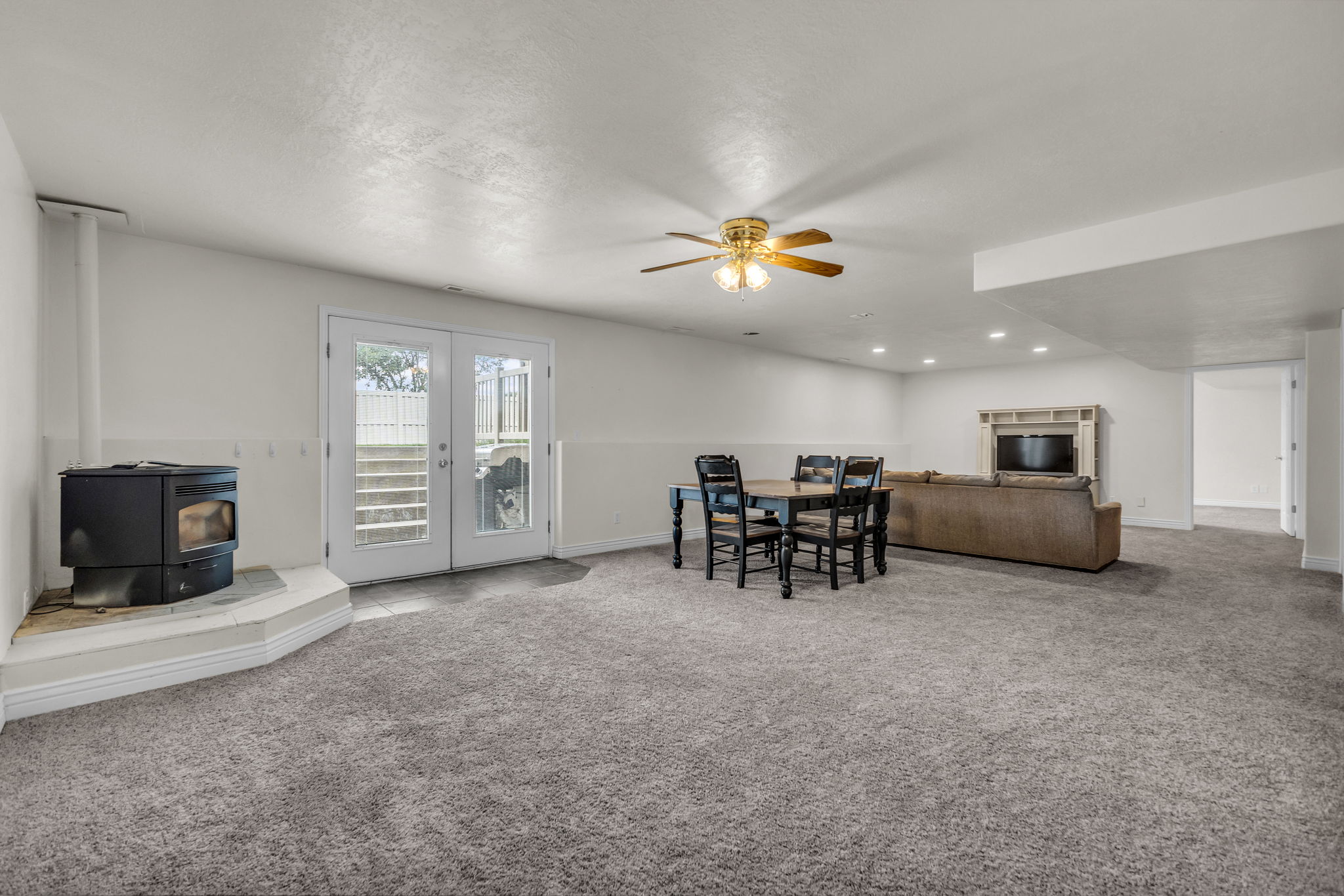 Spacious carpeted room featuring a corner wood-burning stove, white wainscoting, and French doors leading to exterior stairs