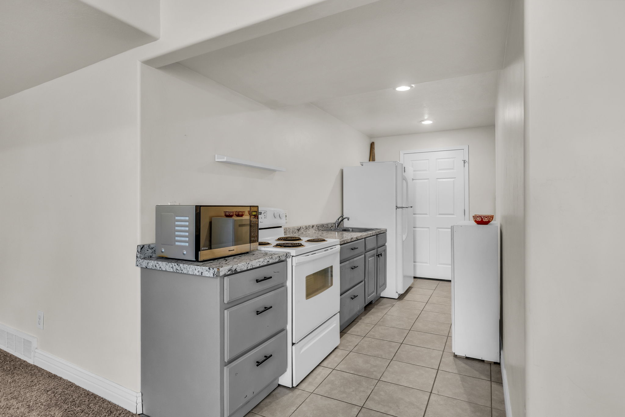 Compact kitchen space featuring light gray cabinetry, speckled countertops, a white electric range, and a white refrigerator