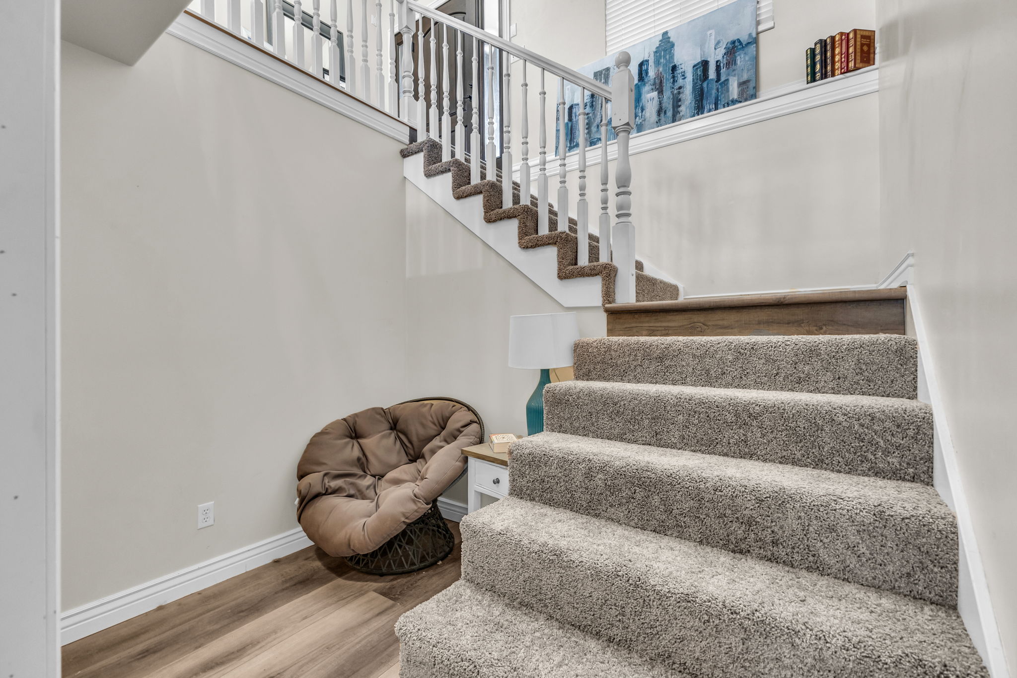 Carpeted staircase with white balusters and wood-finish handrail, featuring wood-finish flooring at the base