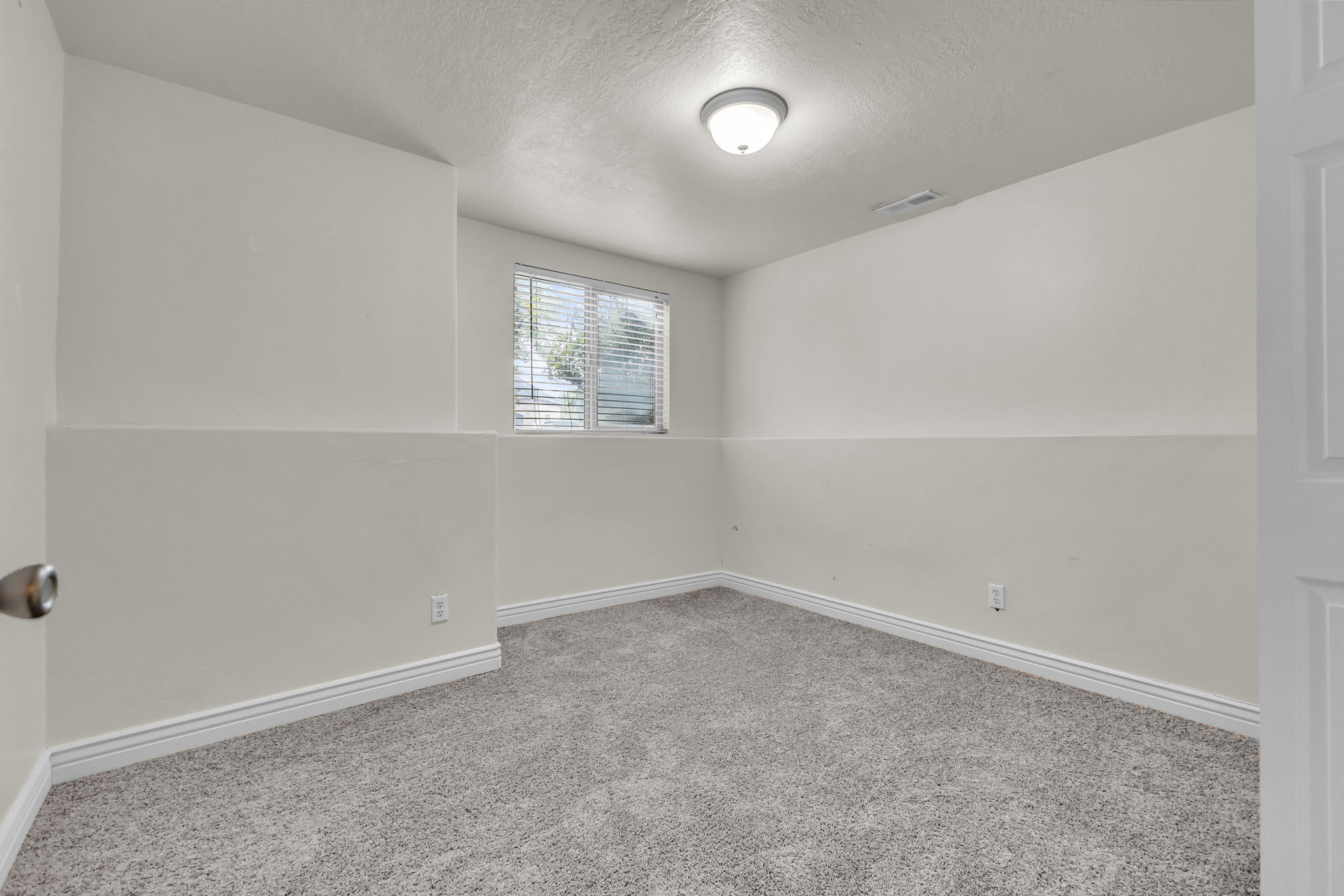 Carpeted room featuring a window with blinds, white trim, and a flush-mount ceiling light fixture
