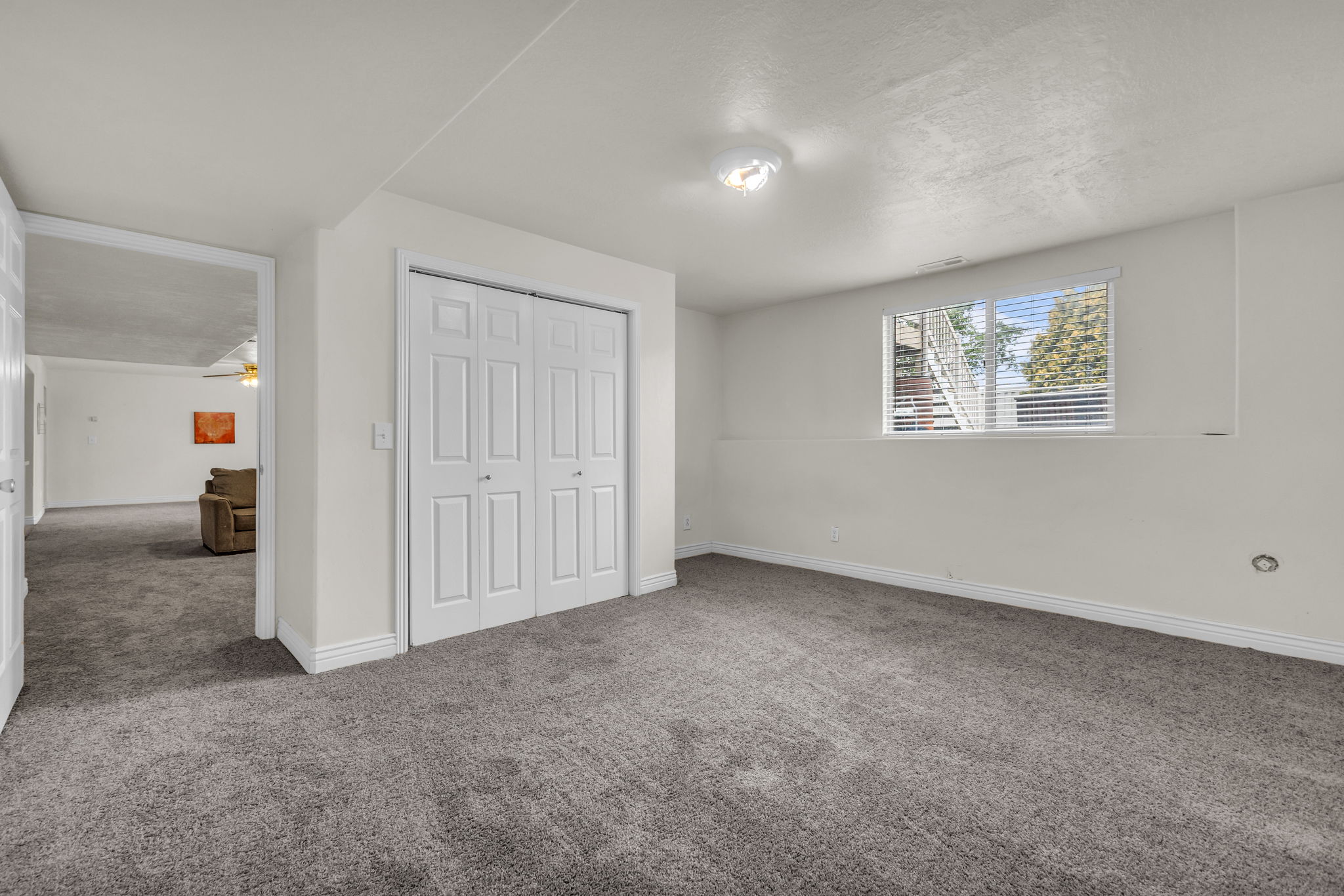 Spacious room featuring neutral carpeting, white walls, a built-in closet with bifold doors, a window with blinds, and recessed lighting