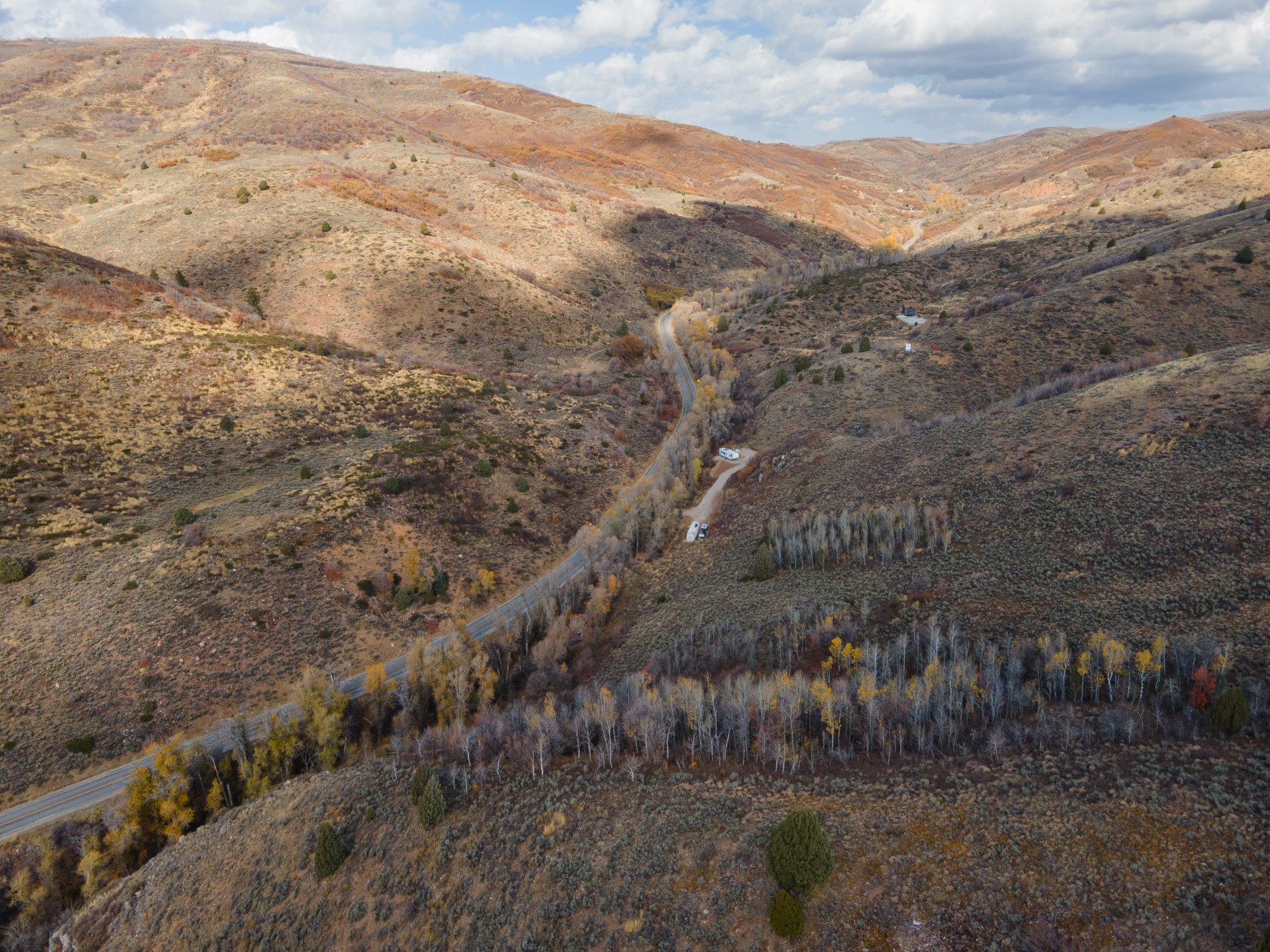 Expansive mountain landscape featuring a winding road, natural terrain, and scattered trees