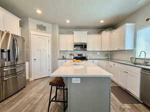 Kitchen featuring a central island with a light-toned countertop, white cabinetry, stainless steel appliances, subway tile backsplash, and wood-finish flooring