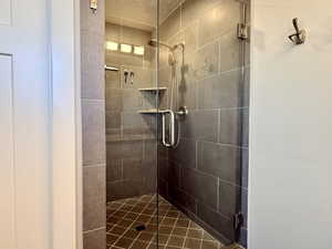 Walk-in shower featuring glass enclosure, dark gray tile walls, geometric tile flooring, built-in shelving, and a rain showerhead