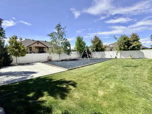 Spacious backyard featuring a manicured lawn, concrete patio, white privacy fencing, and mature trees
