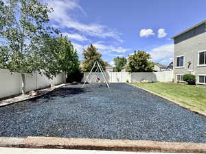 Expansive backyard featuring a dedicated play area with blue rubber mulch and a swing set, bordered by a privacy fence