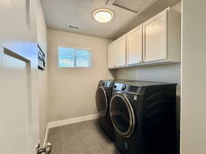 Dedicated laundry space featuring white upper cabinetry, tiled flooring, and a window with blinds