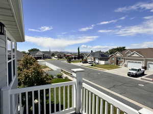Balcony with white railing overlooking a street with residential homes, green lawns, and mature trees