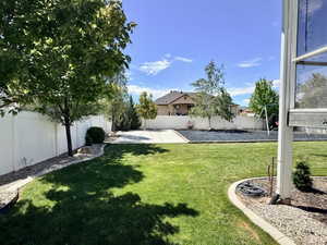 Expansive backyard featuring a green lawn, concrete patio, and a white privacy fence
