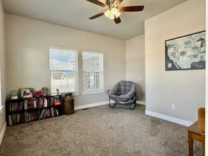 Carpeted interior room featuring two windows with horizontal blinds, a ceiling fan with integrated lighting, and neutral-toned wall paint