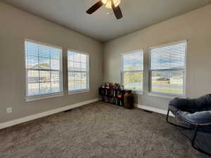 Carpeted room featuring a ceiling fan with integrated lighting, four windows with blinds, and neutral wall tones