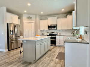 Modern kitchen featuring a light gray island with white countertop, white upper and lower cabinetry, and wood-finish flooring
