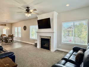 Living area featuring a floor-to-ceiling fireplace with a stacked stone facade and white mantel, a ceiling fan with integrated lighting, recessed lighting, and multiple windows with horizontal blinds