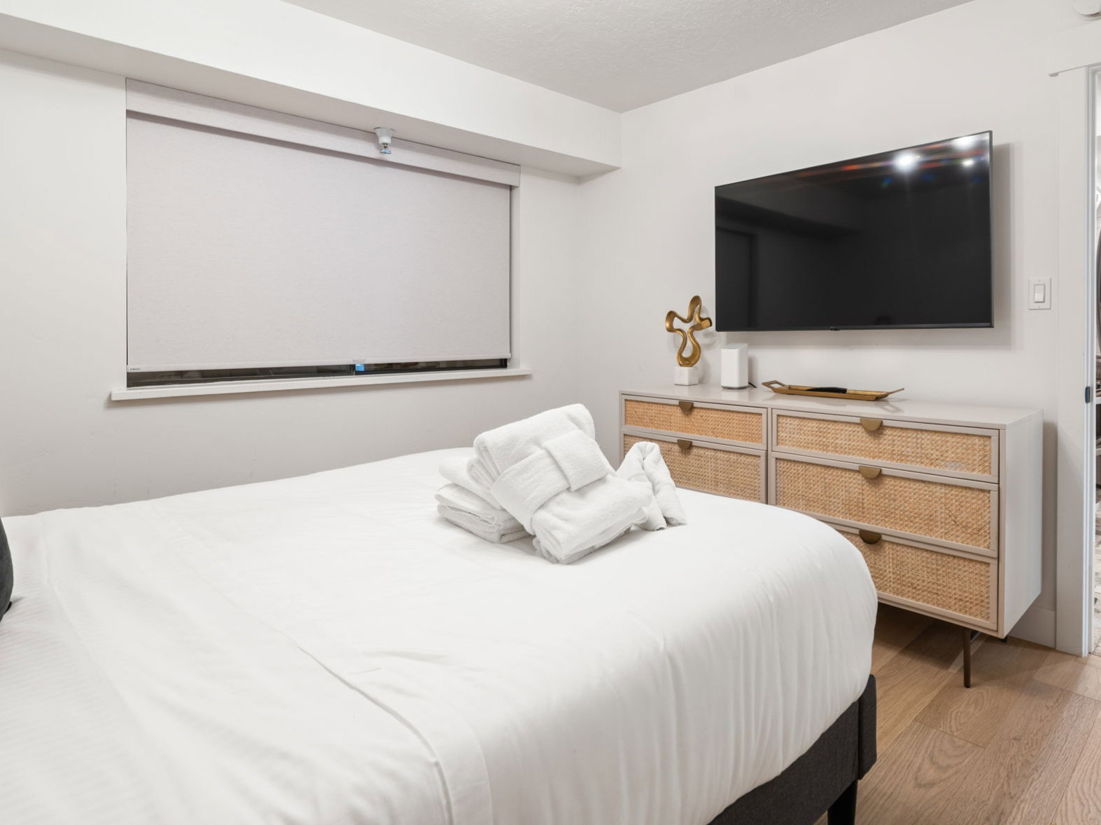 Bedroom featuring a window with a roller shade, wood-finish flooring, and a contemporary light fixture